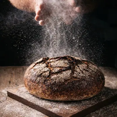 Flaxseed Rye Loaf on a wooden board, flour dusting down from the baker’s hands