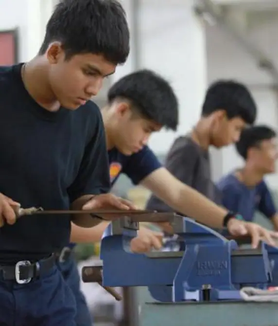 Young men filing a metal bar held in a bench vice during a workshop class