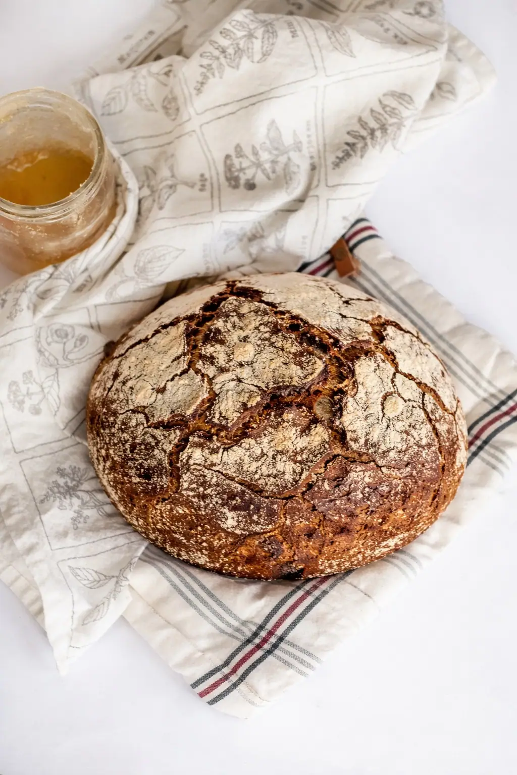 A rye loaf on a linen kitchen towel, next to a jar of honey